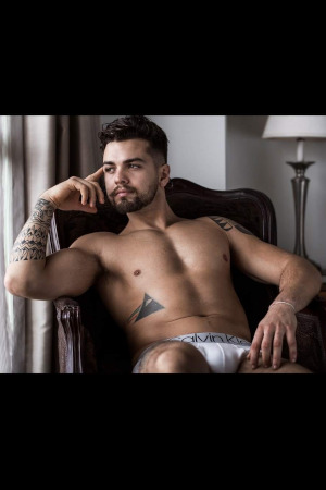 confident looking topless waiter with dark hair and half sleeve tattoo taking it easy in an auckland apartment near ponsonby