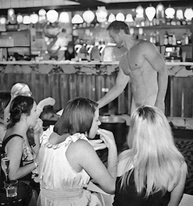 Topless waiter serving drinks to a group of hens at a bar